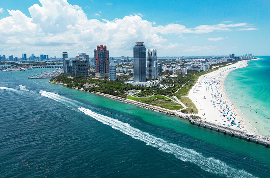 Moving from New Jersey to Florida » Ridgewood Moving Services Aerial view of a tropical coastline with a sandy beach, turquoise water, tall hotels along the shore, and a pier extending into the ocean.