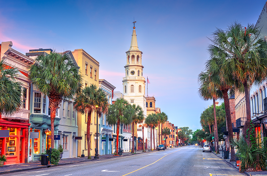 Moving from New Jersey to South Carolina or North Carolina » Ridgewood Moving Services Sunny street in a historic town with colorful storefronts, palm trees, and a tall church spire in the center.