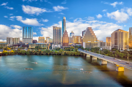 Moving from New Jersey to Texas, Tennessee » Ridgewood Moving Services City skyline along a wide river with a bridge crossing the water; small boats row on the river under a blue sky.
